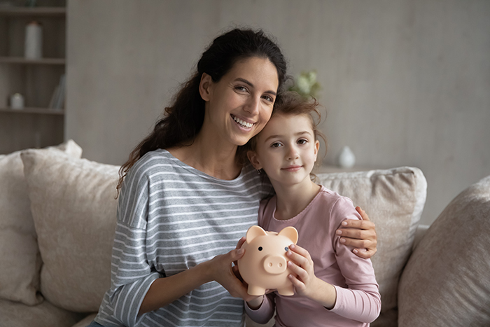 Head shot portrait mother and little daughter holding piggy bank
