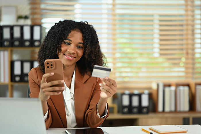 Smiling African American female worker holding mobile phone and credit card for financial transaction